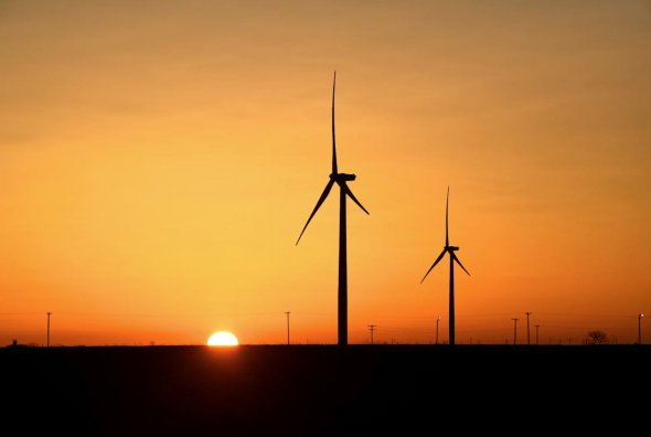 2019年2月12日，美國德克薩斯州大斯普林的二疊紀盆地石油和天然氣生產區，風力渦輪機在日出時運行。